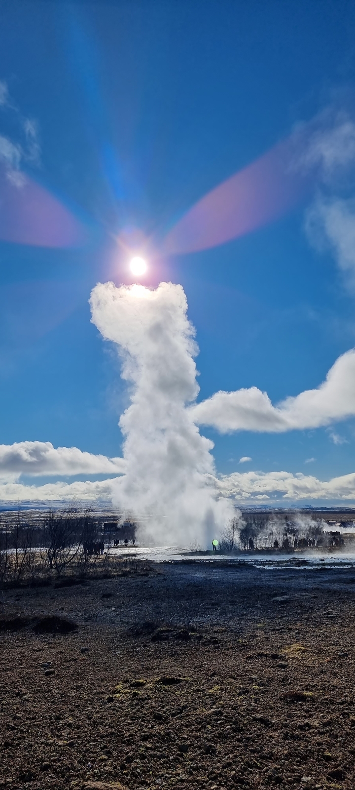 Un geyser en éruption contre un ciel bleu avec des nuages.