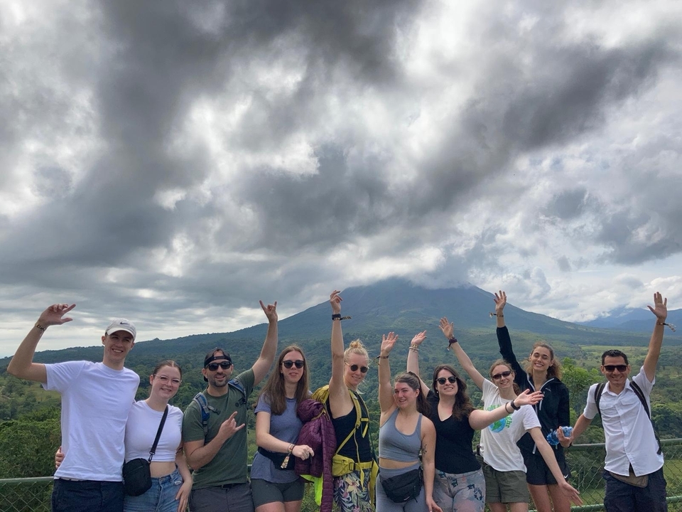Photo de groupe avec des personnes levant les mains devant une montagne.