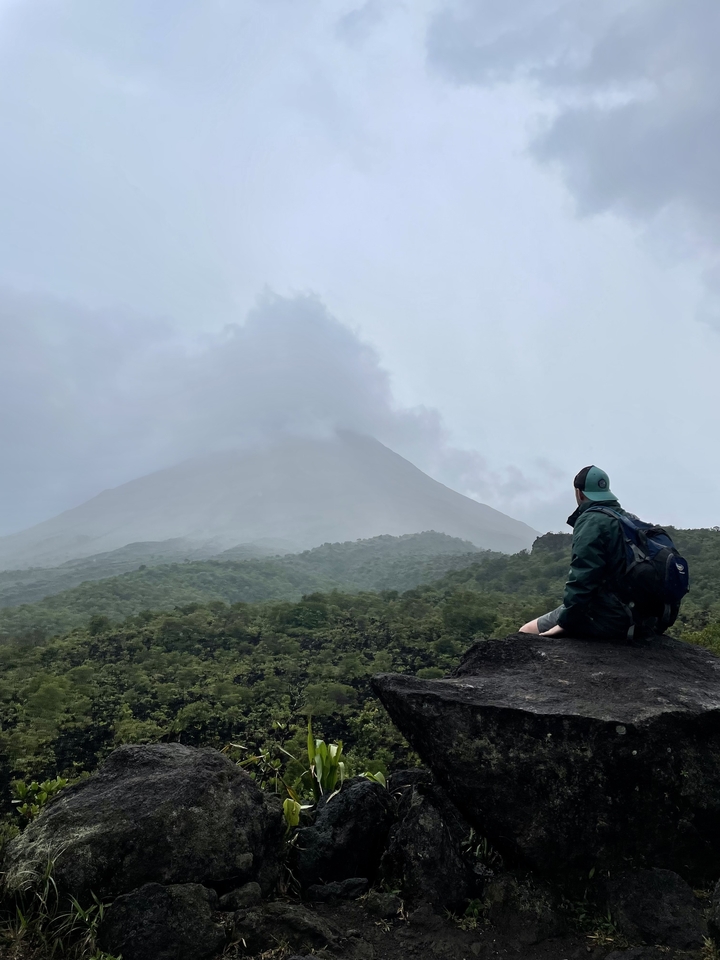 A person sitting on a rock gazing at a volcano in the distance.