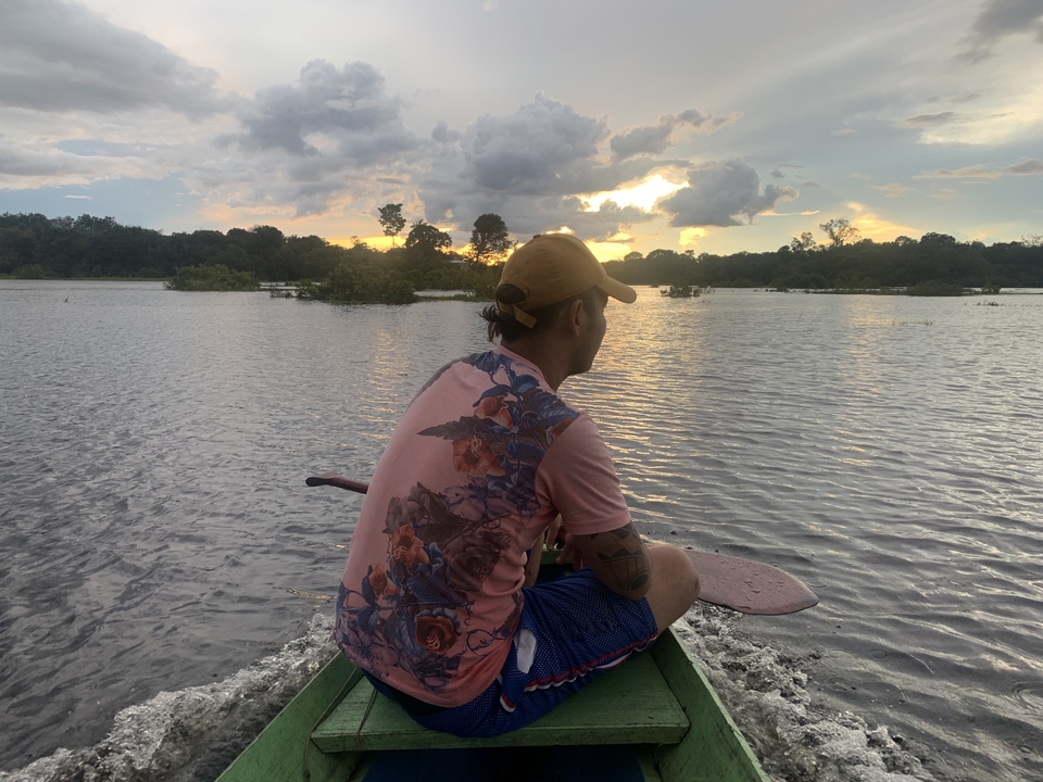 Homme pagayant dans un bateau sur une rivière au coucher du soleil.