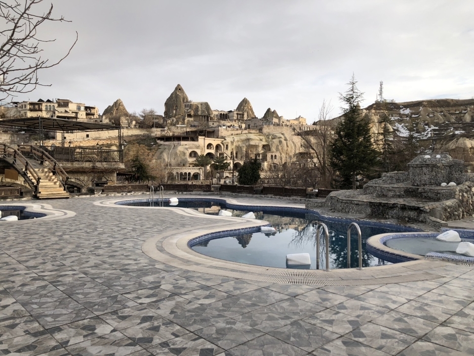 Piscine vide surplombant des formations rocheuses et des hôtels troglodytes.