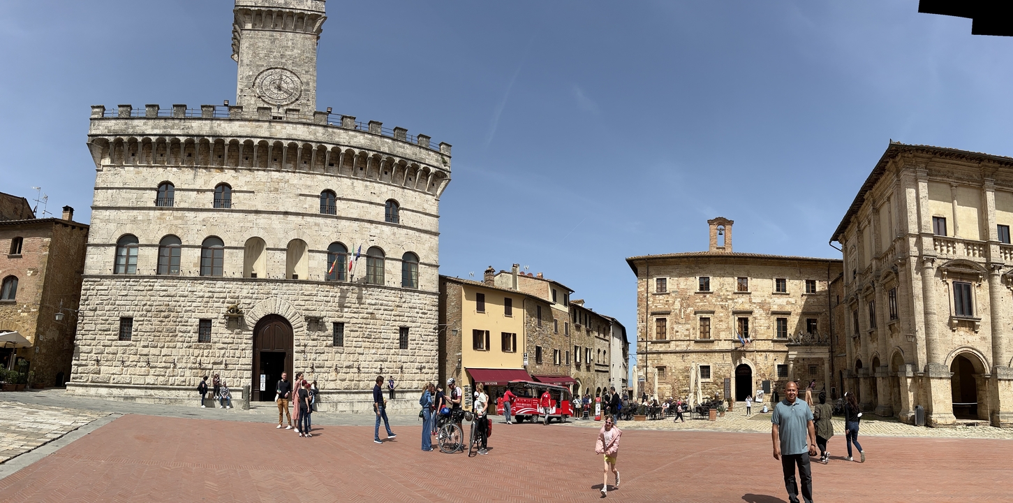 Une place de ville avec des bâtiments historiques et des touristes qui se promènent.