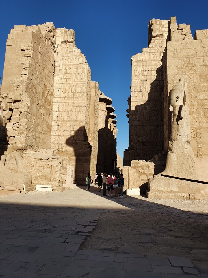 Des visiteurs se promenant dans un ancien temple égyptien avec des statues colossales.