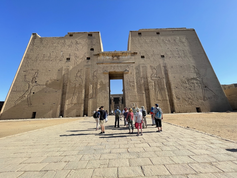 Visiteurs au temple d'Edfou, avec ses murs de pierre massifs ornés de sculptures.
