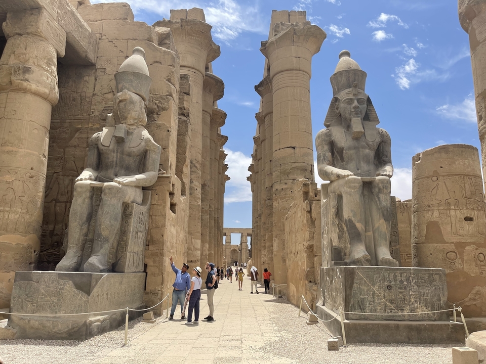 Intérieur du temple de Louxor avec deux statues géantes et des visiteurs.