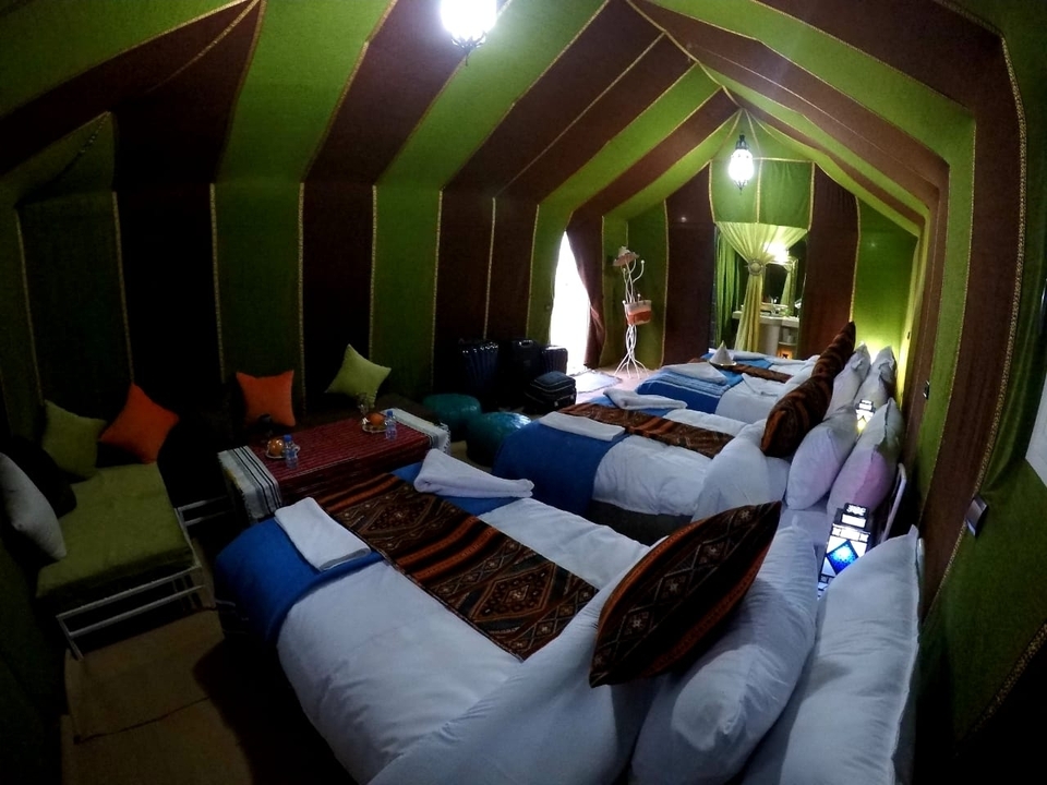 Interior of a colorful Berber-style tent with neatly made multiple beds and patterned textiles.