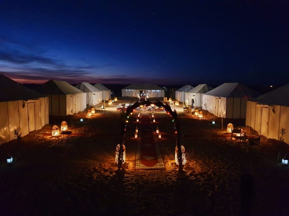 Lantern-lit luxury desert camp lined symmetrically with tents at nightfall.