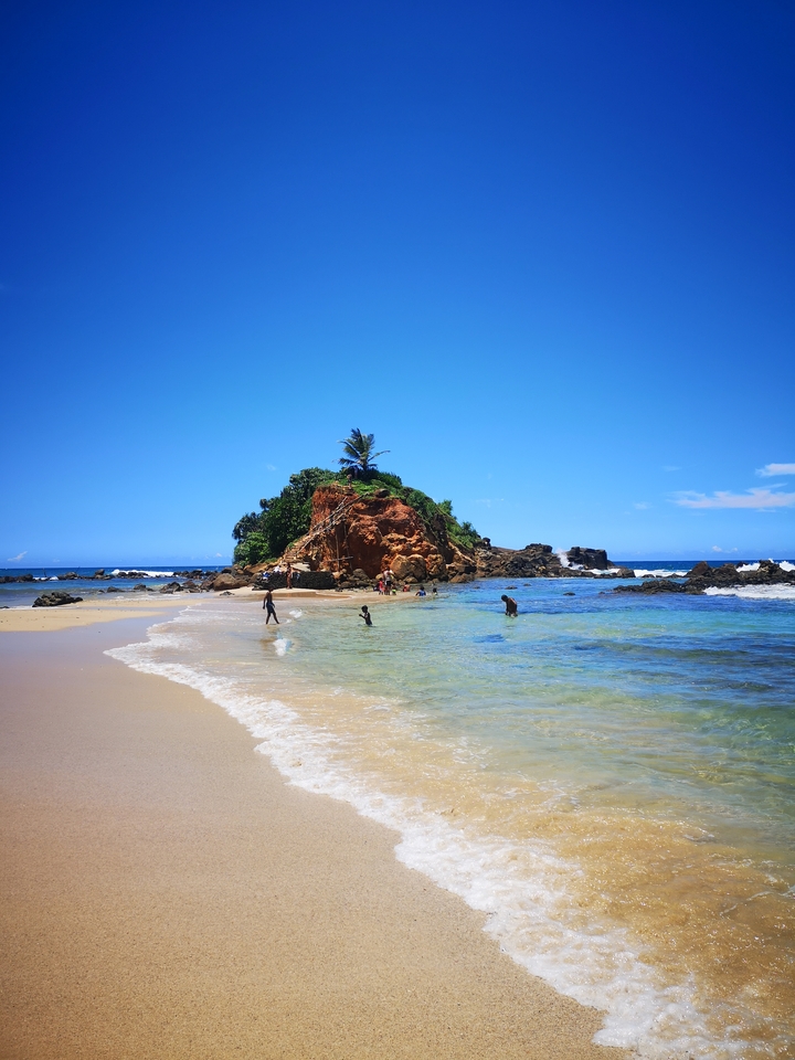 Plage pittoresque avec îlot rocheux et personnes profitant de l'eau