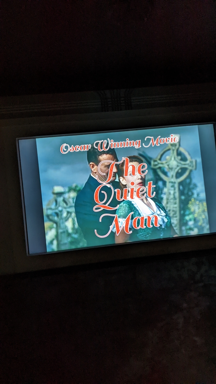 Affiche ou écran montrant le titre d'un film « The Quiet Man ».
Note: "The Quiet Man" is typically left in English as it's the original title of the famous 1952 John Ford film. However, if you need the French release title, it would be "L'Homme tranquille."