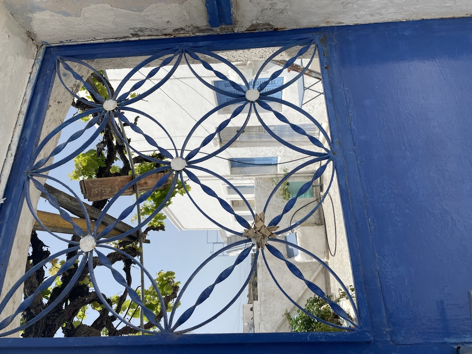 Portail bleu orné avec vue sur un bâtiment blanc en Grèce.