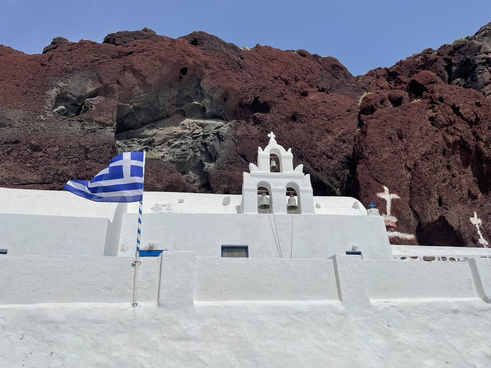 Une église grecque avec un drapeau proéminent et un clocher située dans un paysage rocheux.