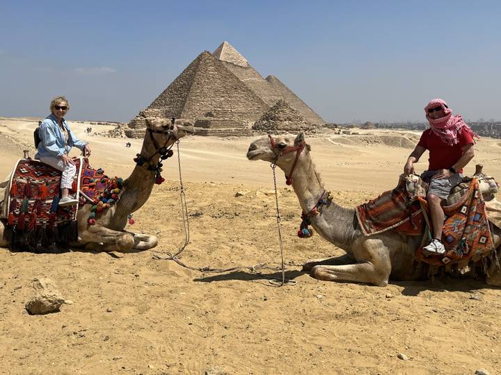 Touristes sur des chameaux avec les pyramides en arrière-plan.