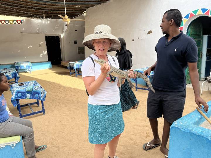 Femme tenant un petit crocodile dans un cadre traditionnel.