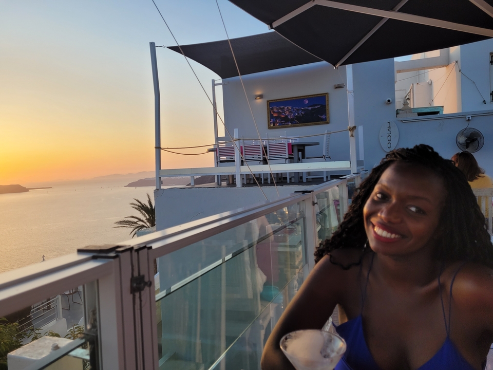 Personne souriante sur un balcon avec vue sur le coucher de soleil.