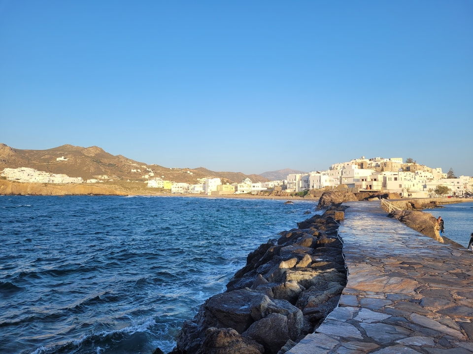 Vue côtière avec rivage rocheux et bâtiments blancs sur mer bleue claire.