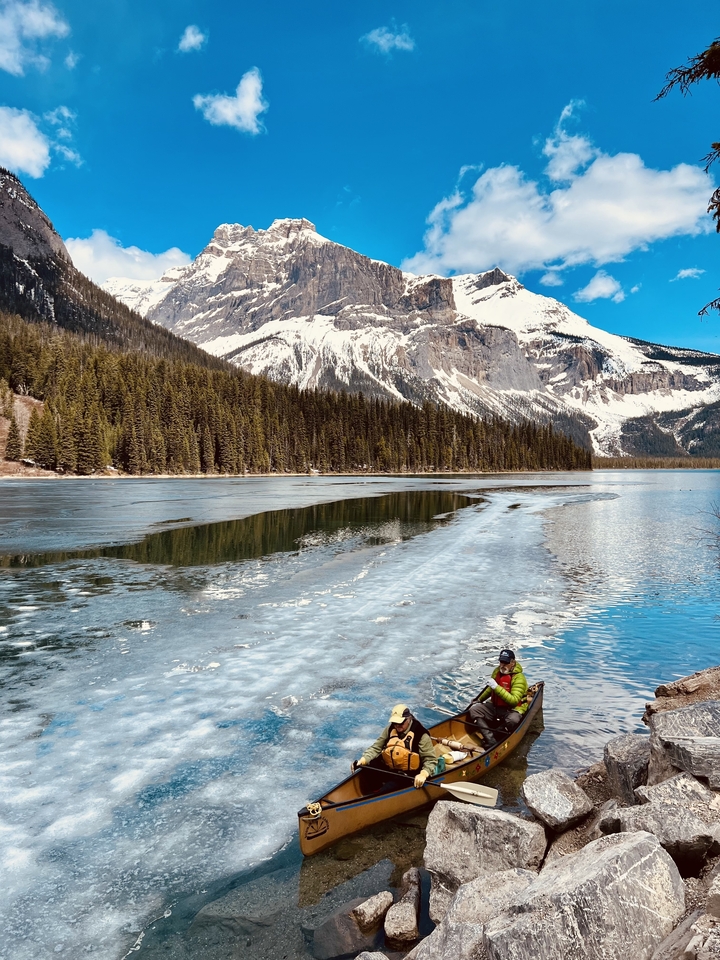 Personne près d'un lac partiellement gelé avec des montagnes enneigées en arrière-plan.