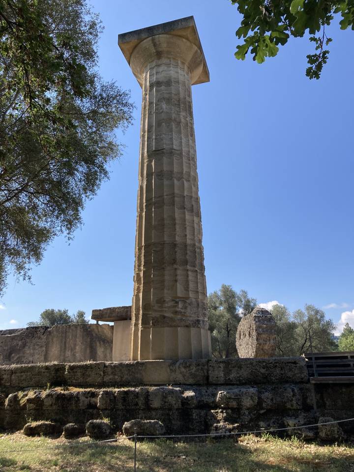 Haute colonne de pierre entourée de verdure dans un parc archéologique.
