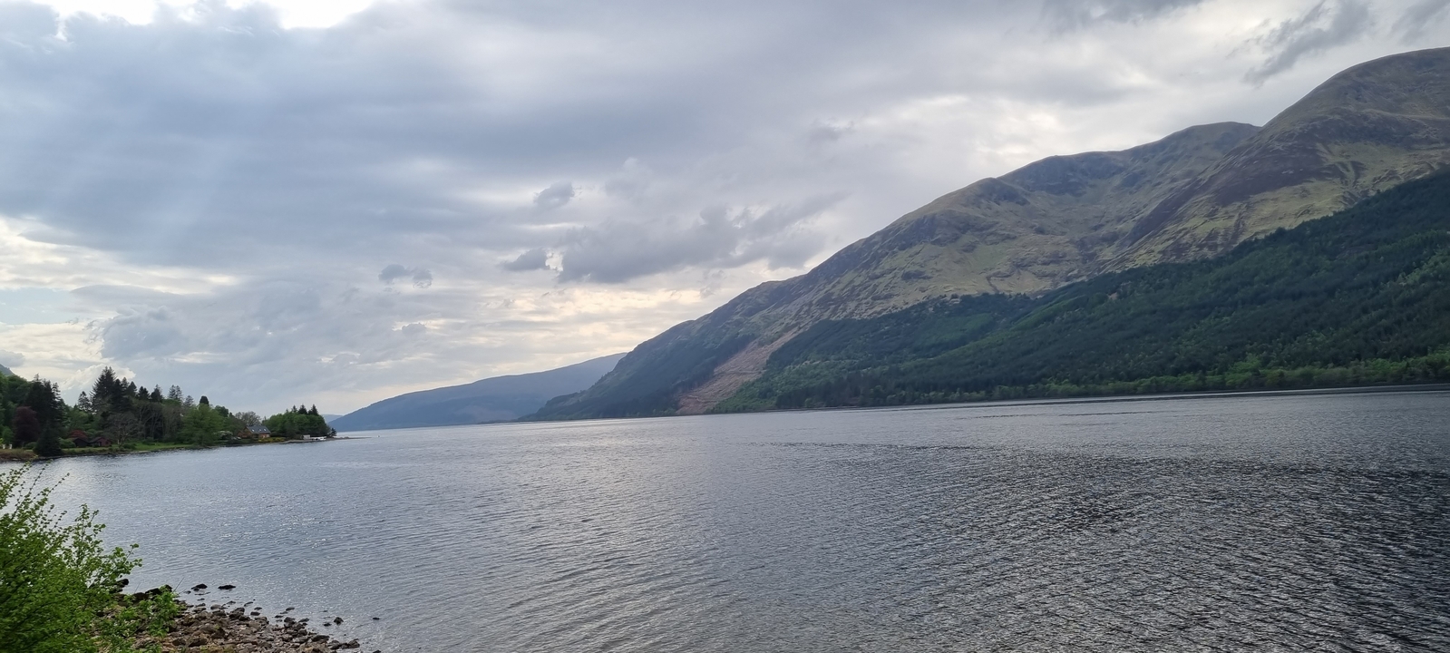 Loch avec des rives boisées et des collines au loin.