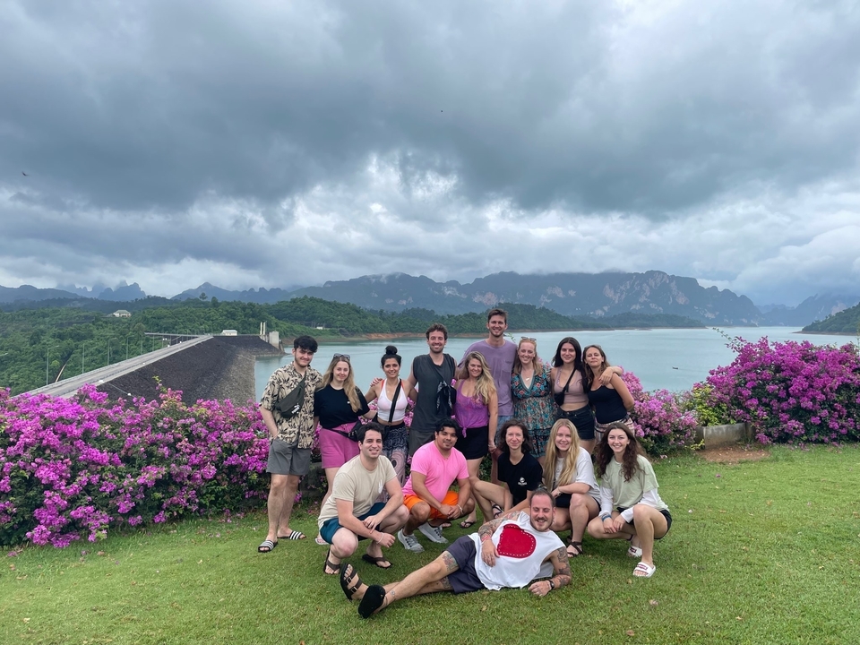 Group of people posing in front of a scenic landscape with water and mountains.