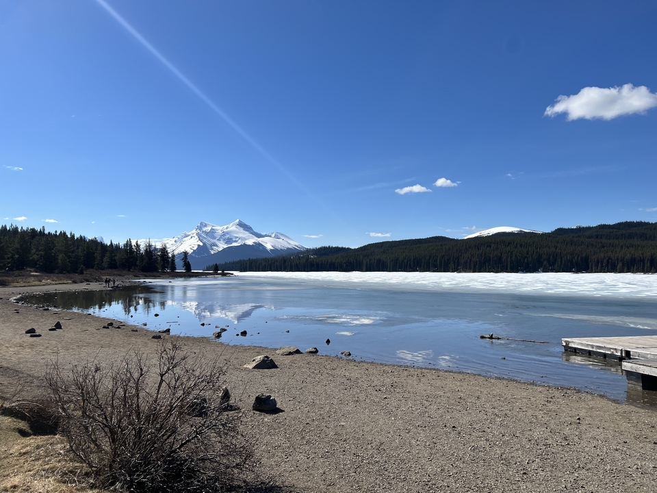 A placid lake with a snowy peak under a clear blue sky.