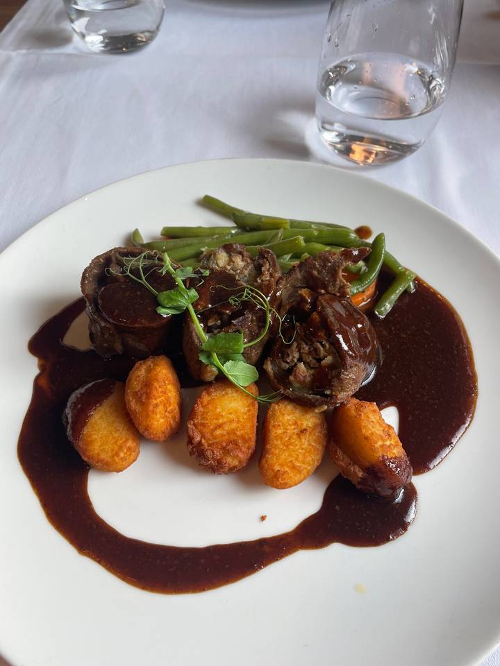 Repas avec de la viande, des pommes de terre et des légumes dans une assiette blanche.