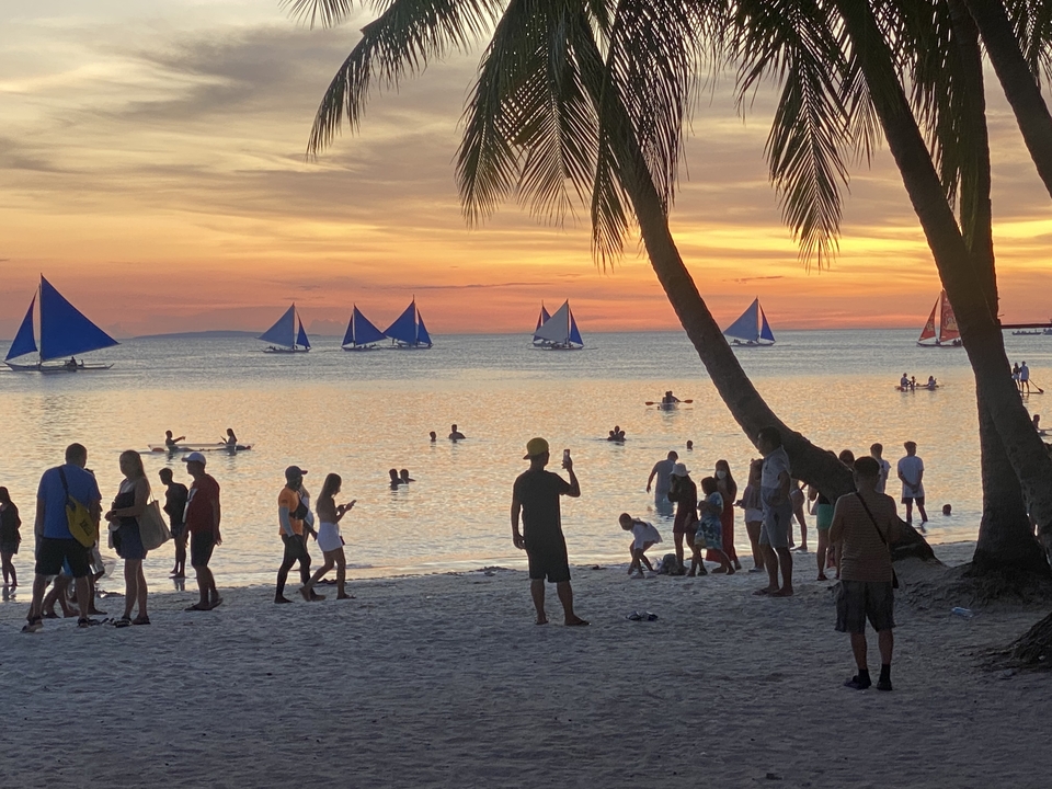 Des gens profitant d'un coucher de soleil à la plage avec des voiliers.