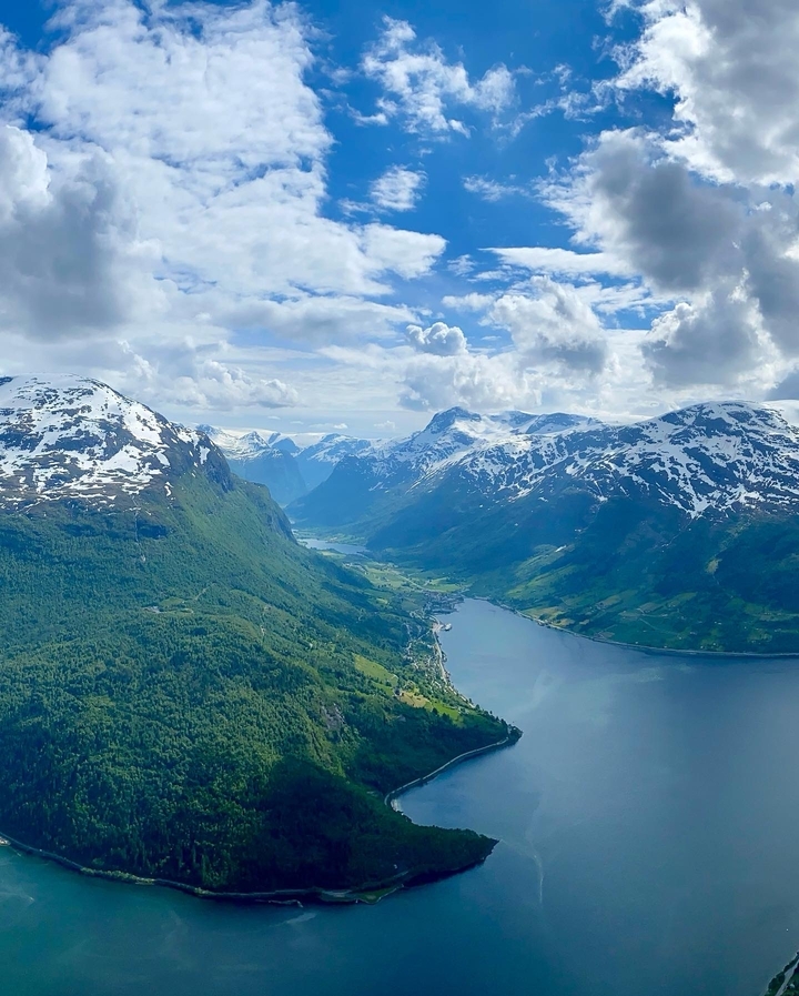 Spectacular aerial vista over snow-capped Norwegian fjord mountains and a deep blue inlet stretching into the distance.