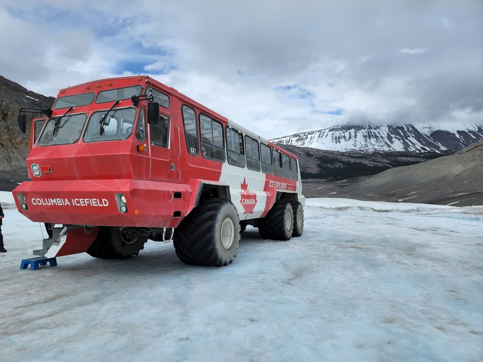 Grand autobus sur un paysage enneigé avec des montagnes en arrière-plan.