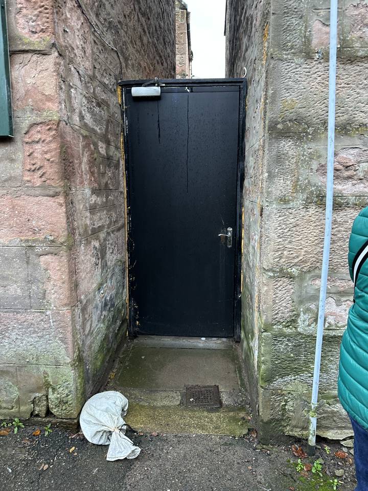 Entrée extérieure avec murs en pierre et quelques objets éparpillés dehors.