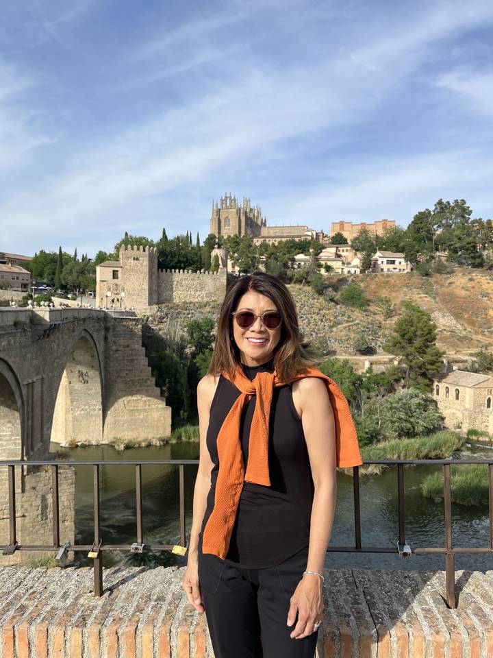 Femme souriante sur un pont de pierre avec une vue sur la ville en arrière-plan.