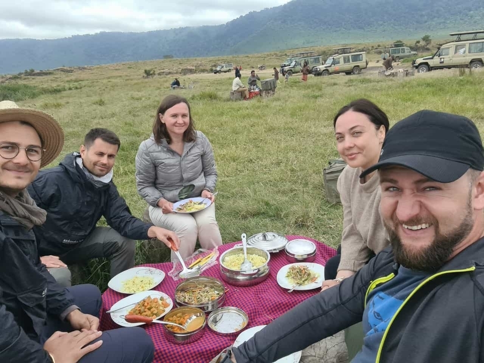 A group of people having a meal on a picnic table in a grassy area.