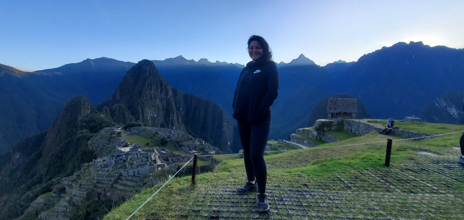 Une personne qui pose avec le Machu Picchu en arrière-plan sous un ciel bleu éclatant.