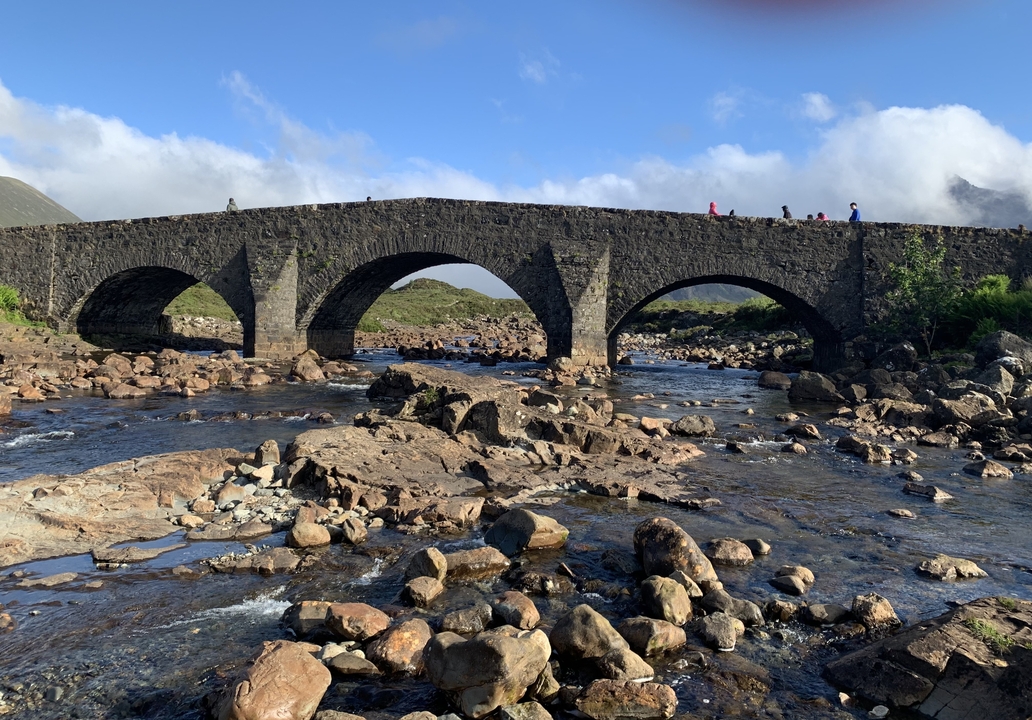 Pont de pierre au-dessus d'une rivière avec des gens qui traversent, entouré d'un paysage rocheux.