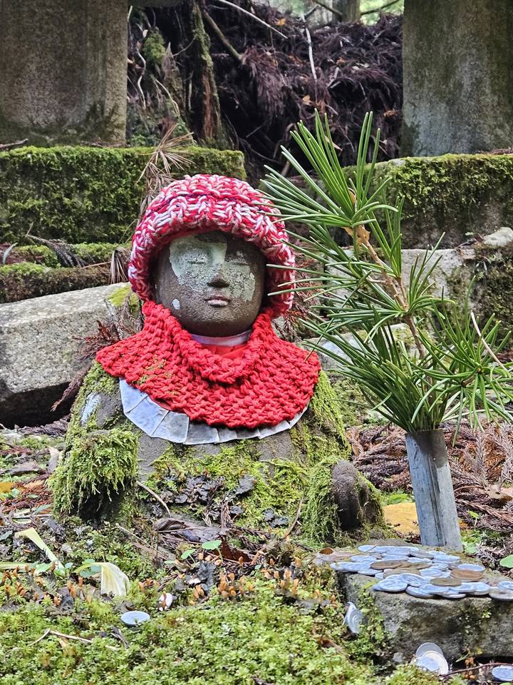 Statue avec un bonnet tricoté rouge et un châle dans une zone moussue.