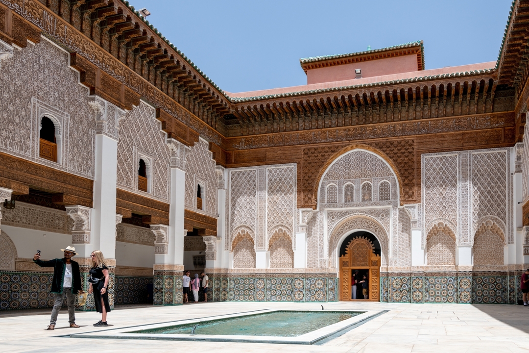 Des gens visitant une cour intérieure richement décorée avec des arches et des carreaux.