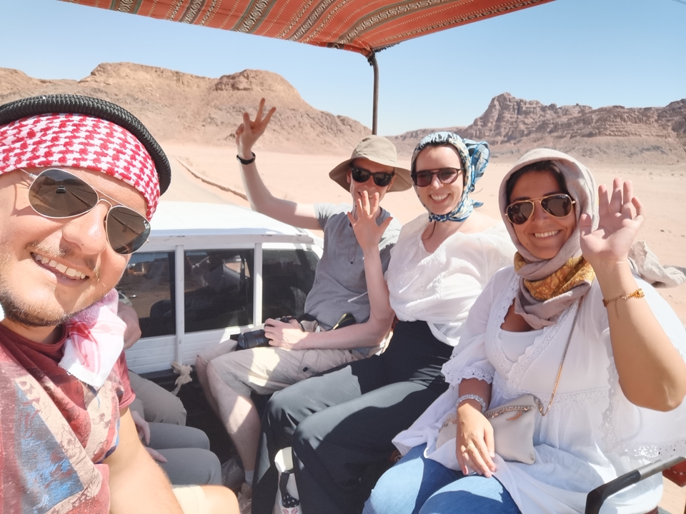 Groupe de personnes souriantes qui saluent de la main dans un véhicule du désert.