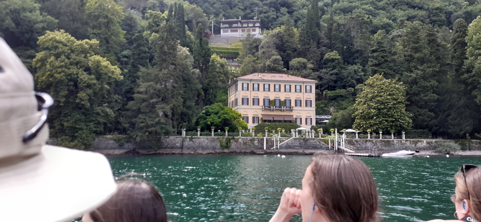 Des personnes profitant d'une promenade en bateau le long d'un lac avec une villa en arrière-plan.