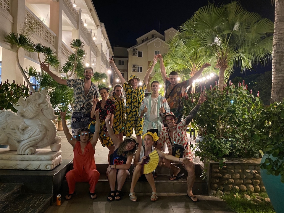 Un groupe de personnes posant avec les mains levées dans un cadre tropical la nuit.