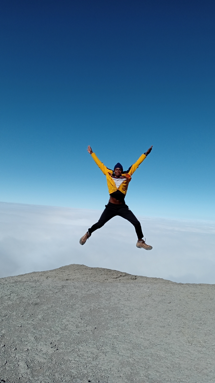 Une personne sautant de joie au-dessus des nuages sur un sommet de montagne.