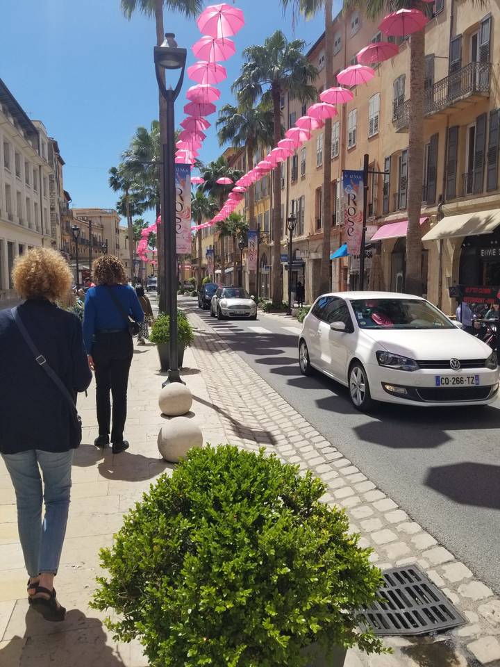 Scène de rue avec des décorations roses et des voitures ; des gens qui marchent.