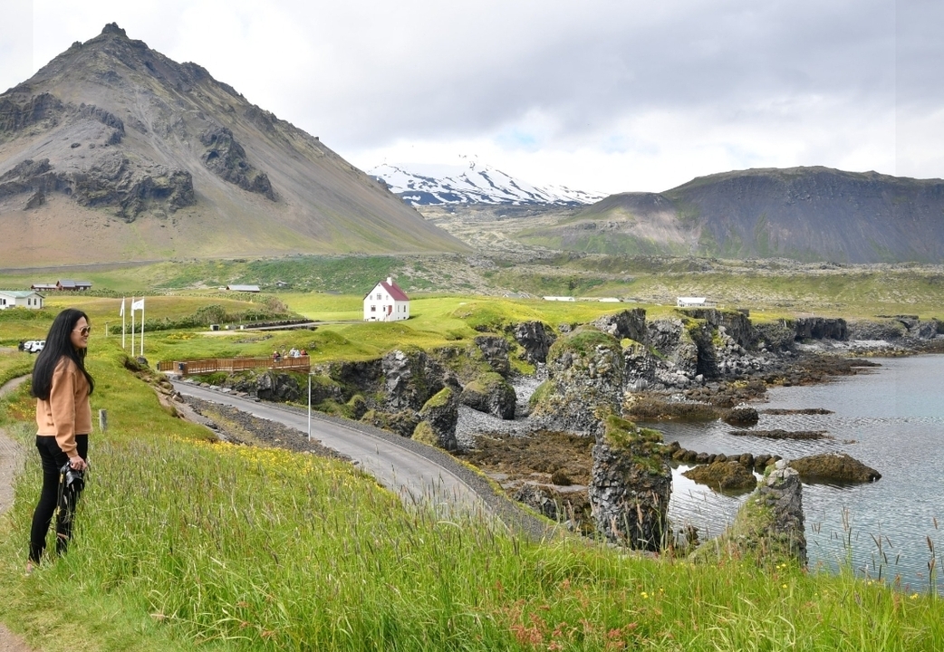 Femme debout sur une falaise herbeuse surplombant la mer avec des montagnes.