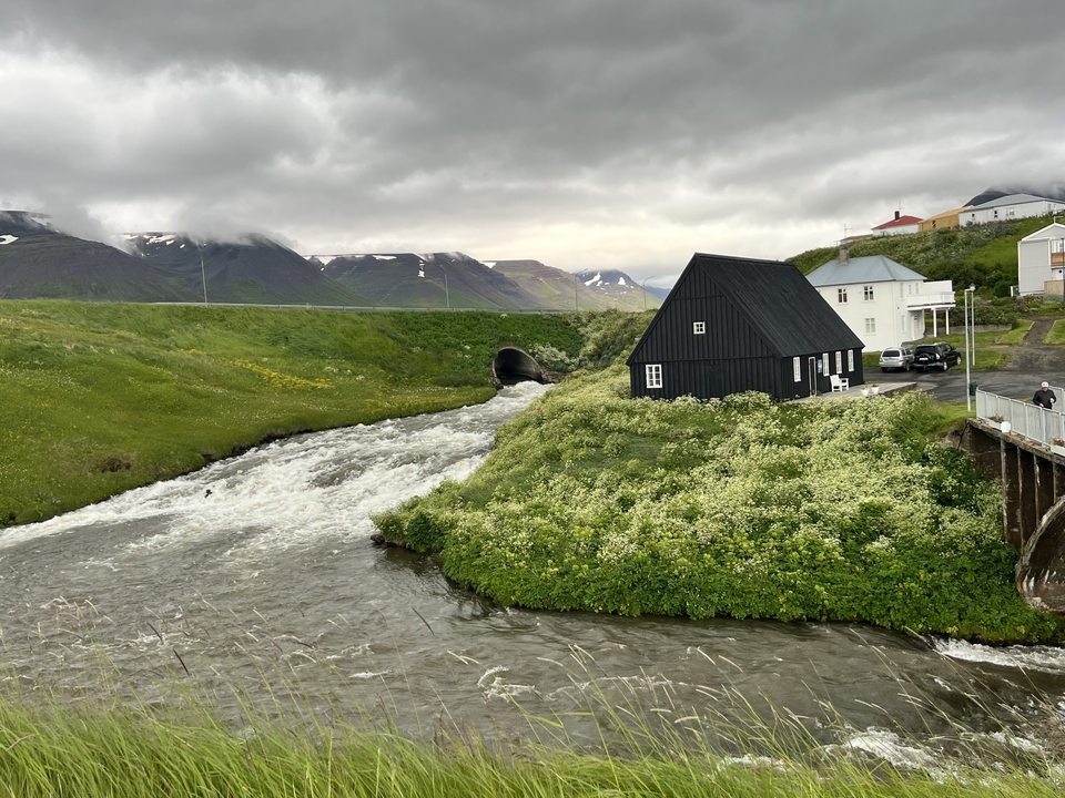 A black house by a river surrounded by green landscape.