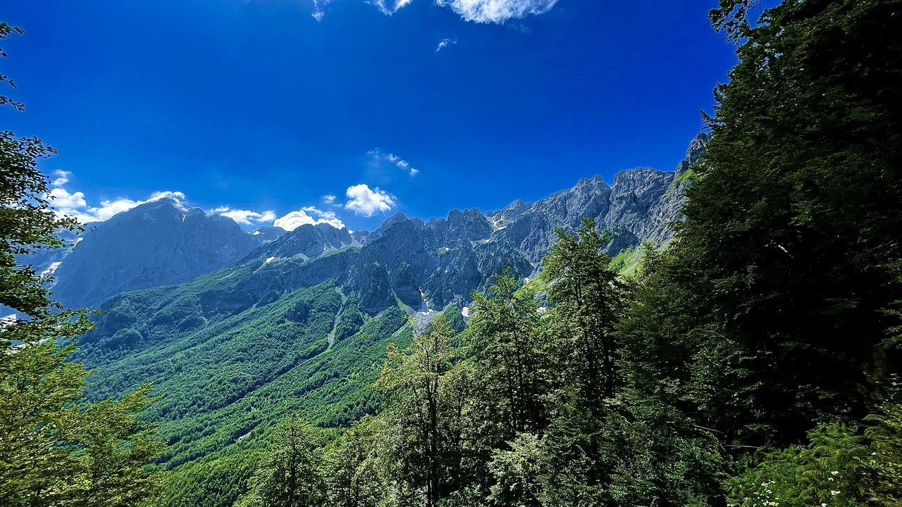 Expansive vista of jagged Albanian Alps with lush green slopes under a vivid blue sky