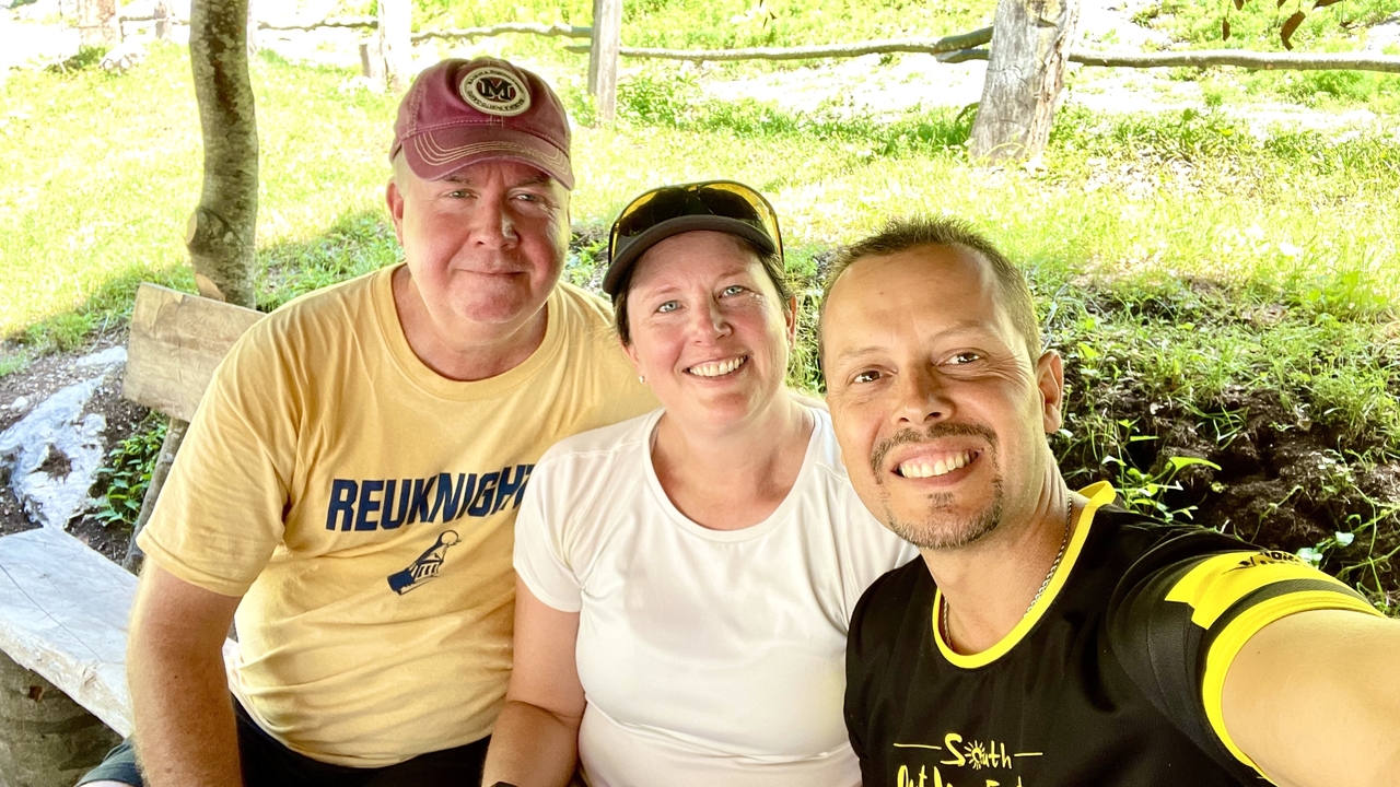 Smiling hikers posing for a selfie break at a shaded wooden rest stop