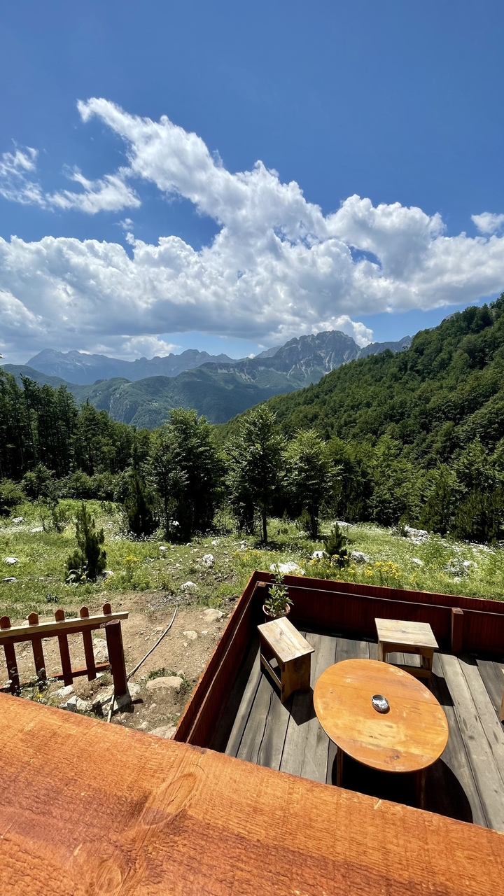 Verdant forested valley with distant craggy peaks under patchy clouds, viewed from a hillside bench