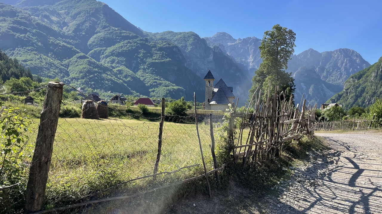 Rustic dirt road lined with wooden fences leading to alpine church and towering mountains