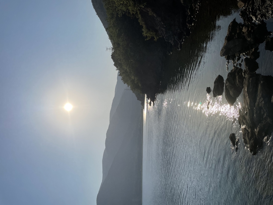 Sun reflecting on calm lake surrounded by hazy mountains in early morning light