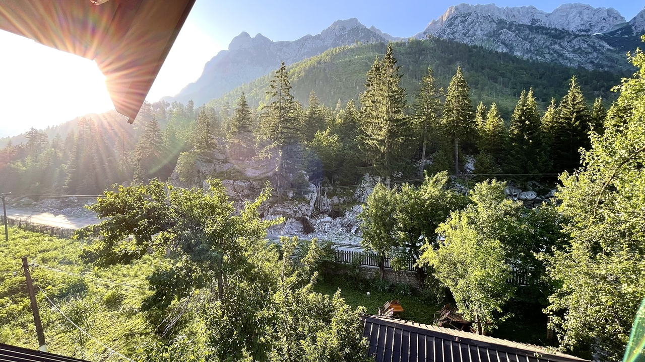 River rushing through a pine-covered valley with dramatic sun rays and high Alpine peaks