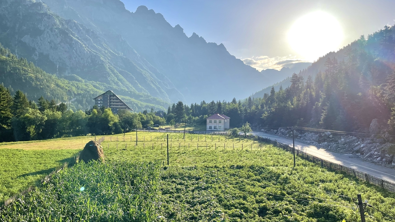 Sun rising over dramatic mountain ridge casting golden light onto a green valley and road