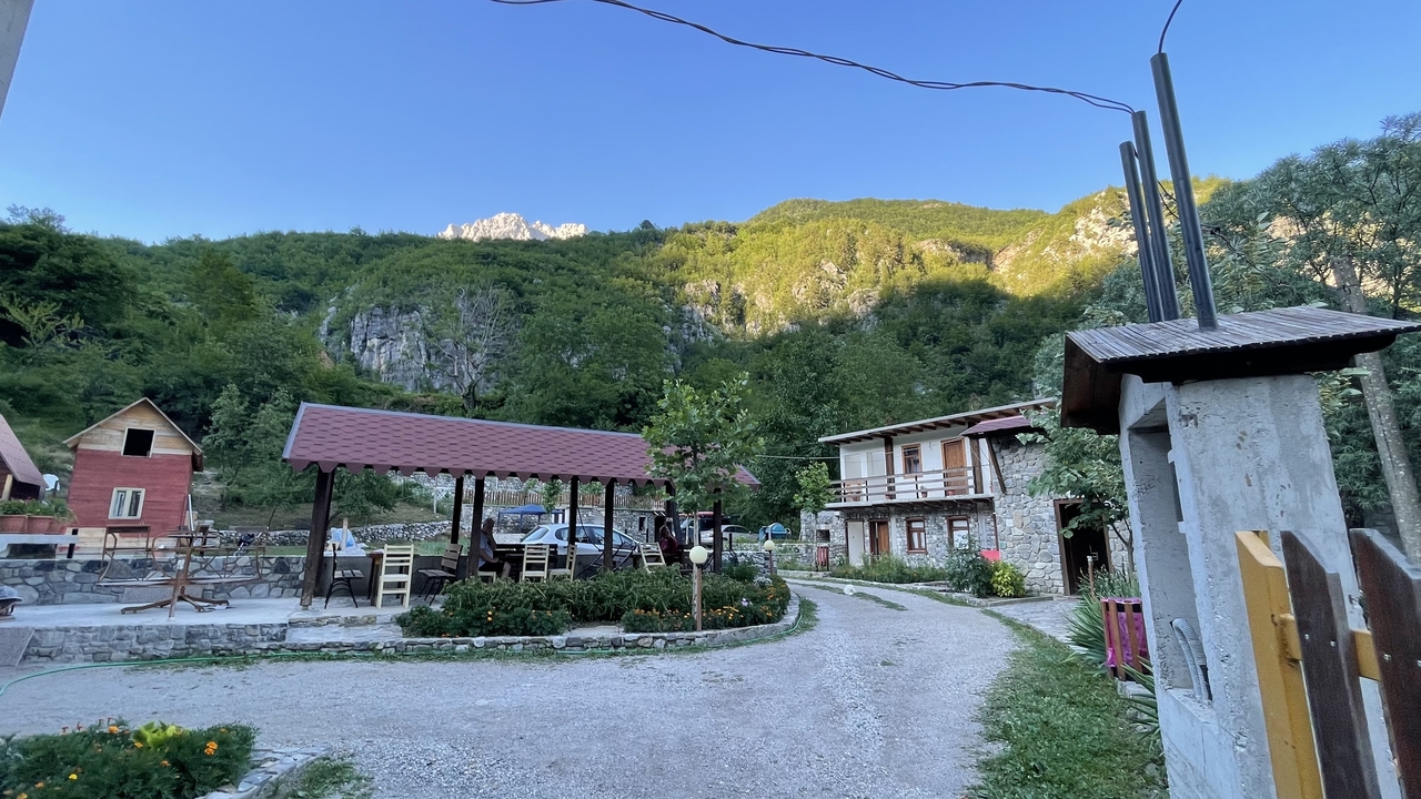 Rural guesthouse courtyard with picnic shelter and flower beds set against forested cliffs